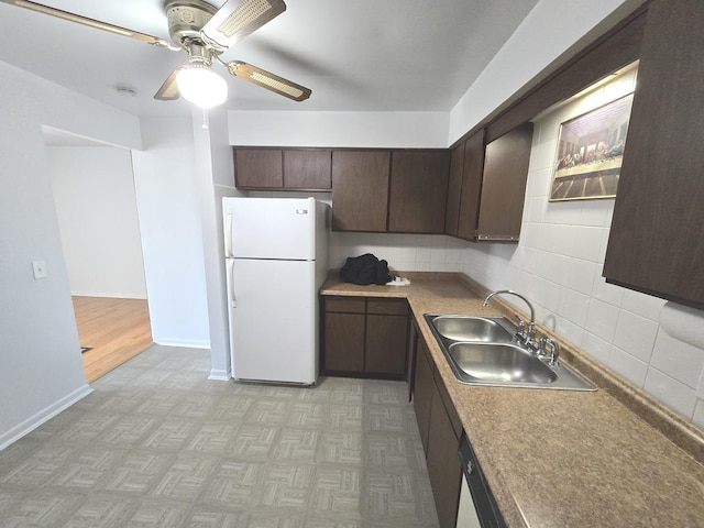 kitchen featuring decorative backsplash, dark brown cabinets, freestanding refrigerator, and a sink