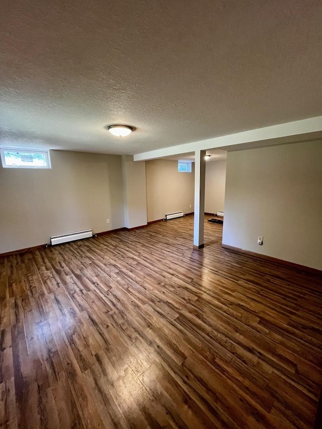 basement featuring a baseboard heating unit, baseboards, dark wood-style flooring, and a textured ceiling