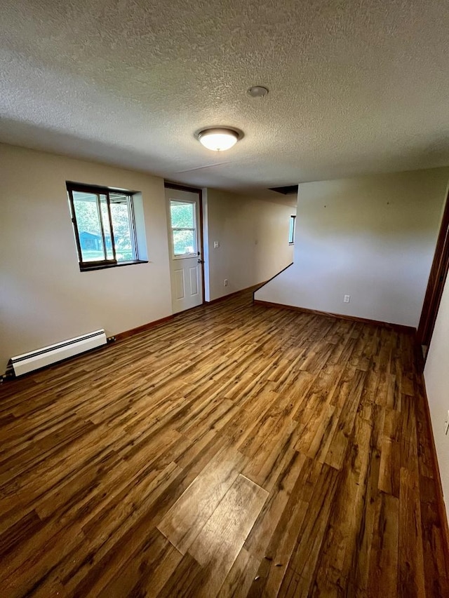 spare room featuring a baseboard heating unit, wood finished floors, baseboards, and a textured ceiling