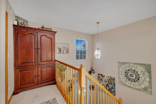 hallway with visible vents, an upstairs landing, and light colored carpet