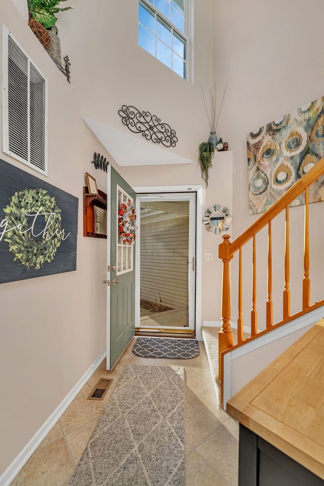 tiled foyer featuring stairs, a high ceiling, baseboards, and visible vents