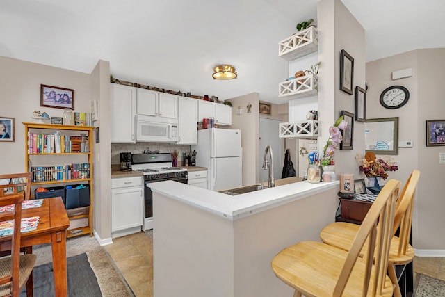 kitchen with tasteful backsplash, white appliances, white cabinetry, and a peninsula