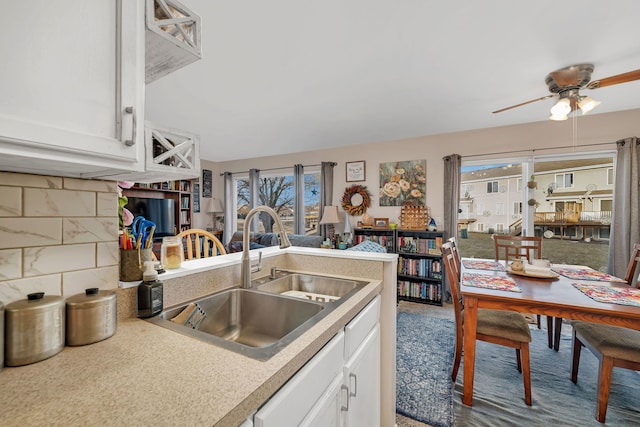 kitchen with backsplash, light countertops, a peninsula, white cabinetry, and a sink