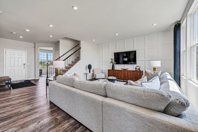 living area featuring baseboards, stairway, recessed lighting, a decorative wall, and dark wood-style flooring