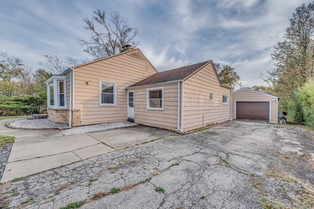 back of property with aphalt driveway, a detached garage, and an outdoor structure