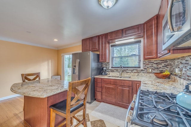 kitchen featuring crown molding, a kitchen bar, decorative backsplash, stainless steel appliances, and a sink