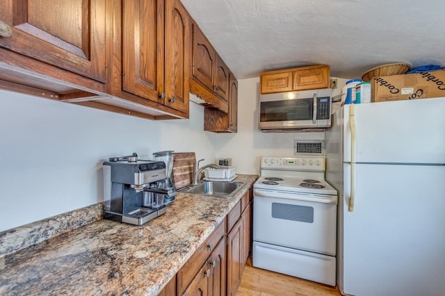 kitchen with light wood-type flooring, brown cabinets, white appliances, a textured ceiling, and a sink