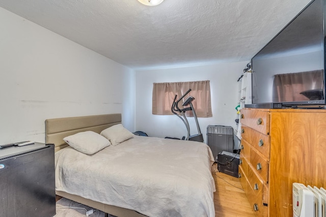 bedroom with radiator heating unit, light wood finished floors, and a textured ceiling