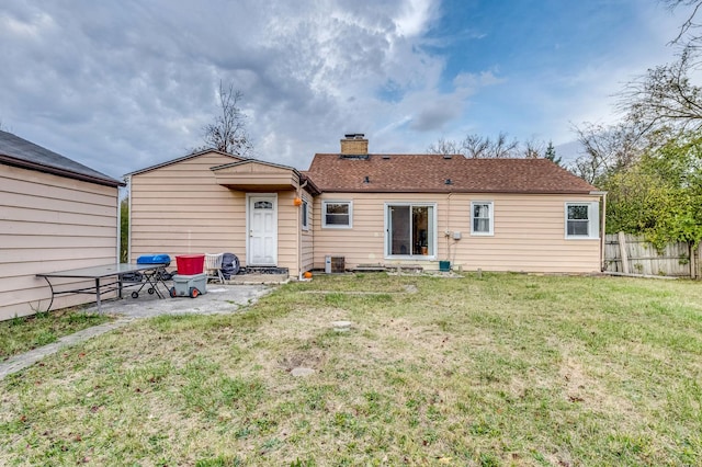 back of house with a shingled roof, fence, a lawn, a chimney, and a patio