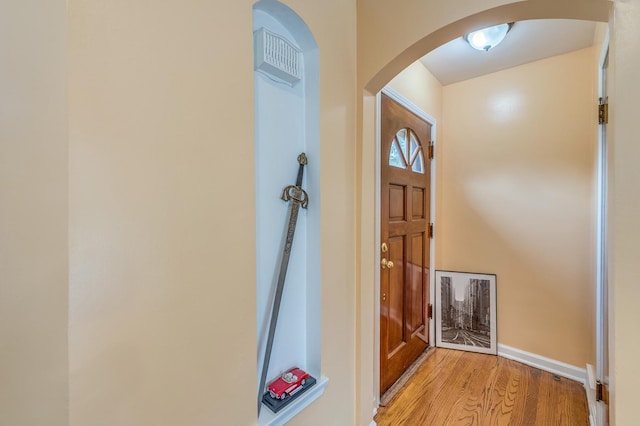 doorway to outside with arched walkways, light wood-type flooring, and baseboards