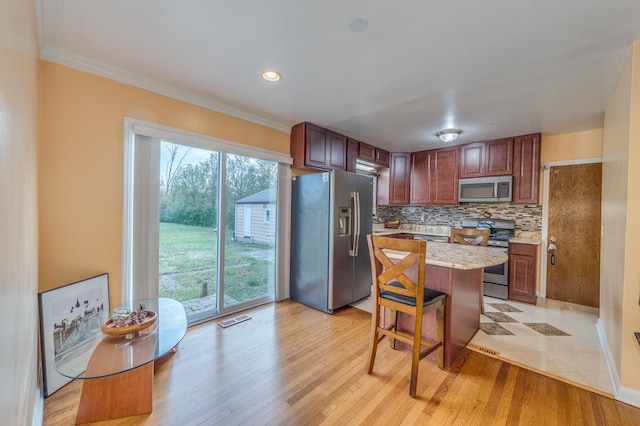 kitchen featuring light stone counters, backsplash, appliances with stainless steel finishes, and light wood-style floors