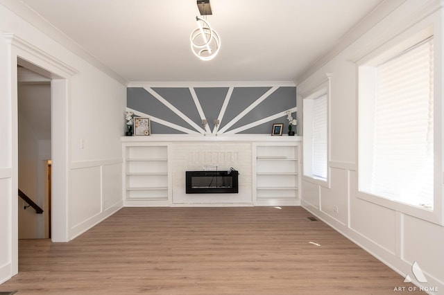 unfurnished living room with light wood finished floors, lofted ceiling, ornamental molding, a fireplace, and a decorative wall