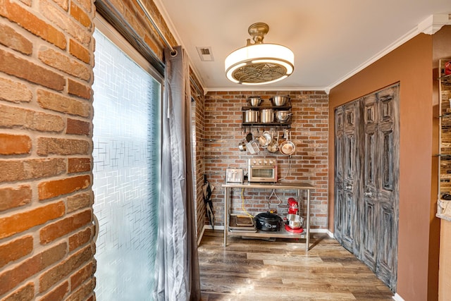 interior space with visible vents, wood finished floors, ornamental molding, and brick wall