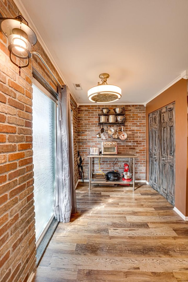 corridor with wood finished floors, baseboards, visible vents, brick wall, and ornamental molding