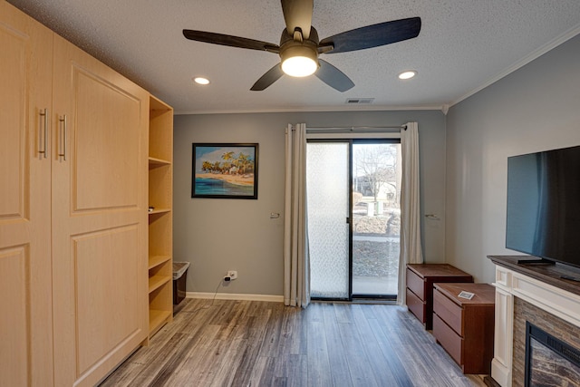 interior space featuring wood finished floors, visible vents, ornamental molding, a stone fireplace, and a textured ceiling