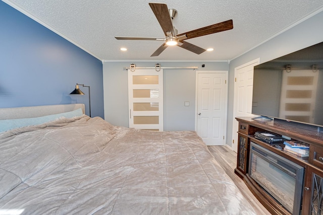 bedroom with wood finished floors, ceiling fan, crown molding, a textured ceiling, and a barn door