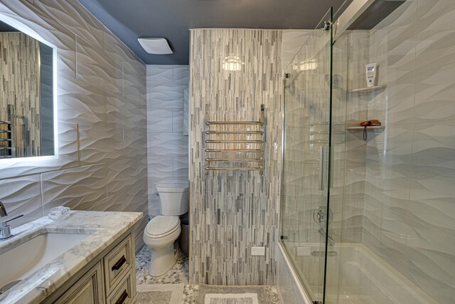 full bathroom featuring vanity, tile walls, toilet, and combined bath / shower with glass door