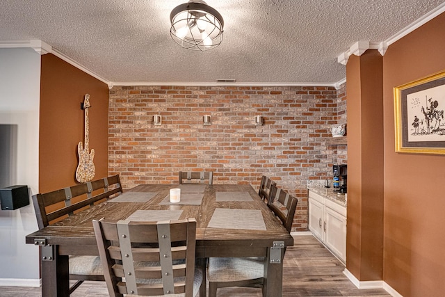 dining space with a textured ceiling, brick wall, ornamental molding, and dark wood-style flooring