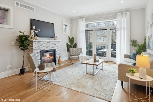 living room featuring wood finished floors, visible vents, baseboards, and ornamental molding