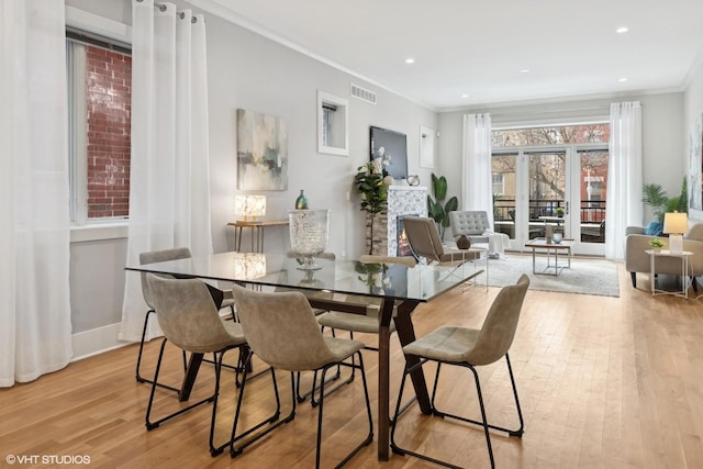 dining space featuring visible vents, light wood-style flooring, recessed lighting, a lit fireplace, and ornamental molding