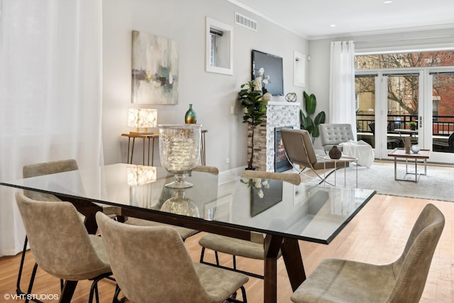 dining room with wood finished floors, a fireplace, visible vents, and ornamental molding