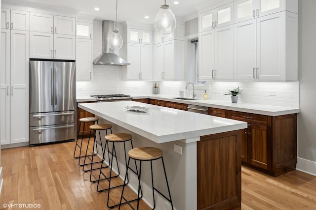 kitchen with a center island, a breakfast bar area, stainless steel appliances, wall chimney exhaust hood, and a sink