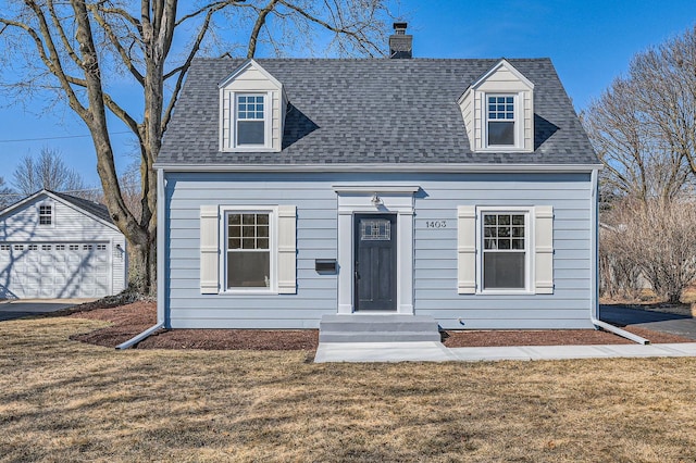 new england style home featuring roof with shingles, an outdoor structure, and a front yard