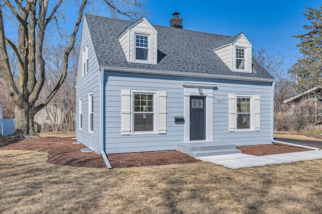 cape cod home with a shingled roof, a front lawn, and a chimney