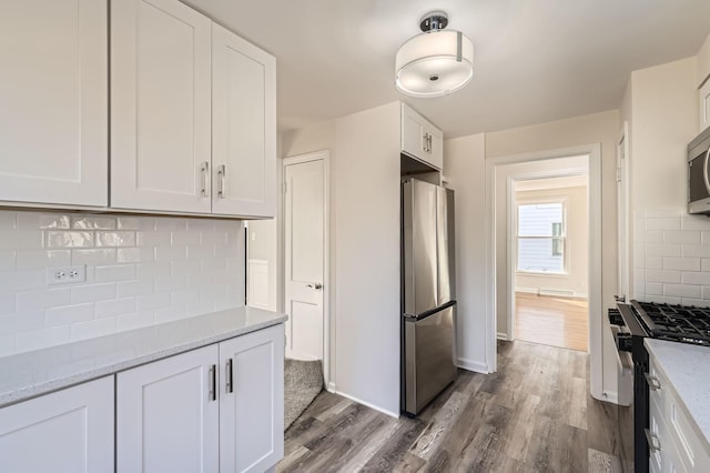 kitchen featuring light stone countertops, dark wood-style flooring, stainless steel appliances, white cabinetry, and backsplash