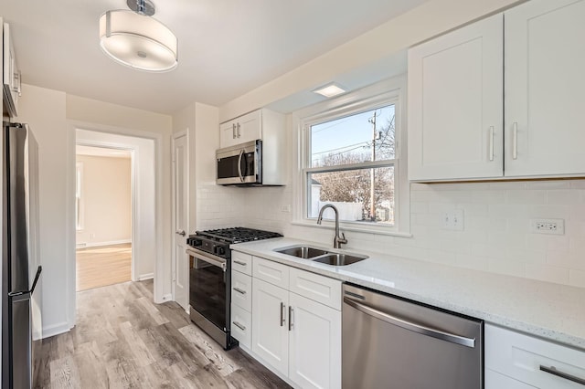 kitchen with tasteful backsplash, appliances with stainless steel finishes, light wood-style floors, white cabinets, and a sink