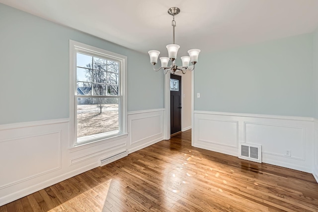 unfurnished dining area with a notable chandelier, visible vents, a wainscoted wall, and wood finished floors