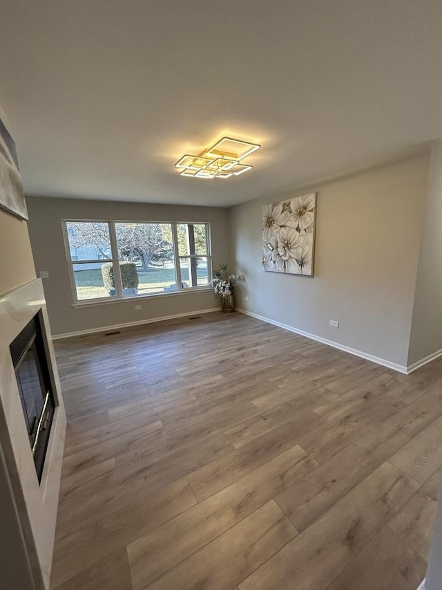 unfurnished living room with a glass covered fireplace, baseboards, and wood finished floors