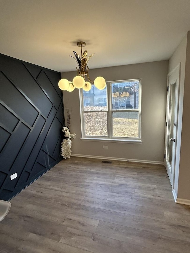 unfurnished dining area featuring a notable chandelier, wood finished floors, visible vents, and baseboards