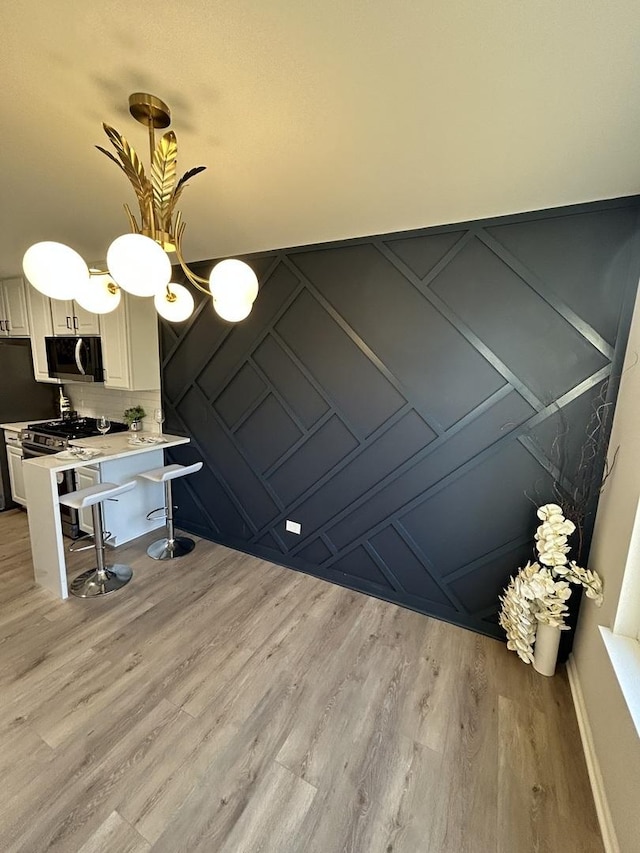 interior space featuring light wood finished floors, stainless steel appliances, light countertops, a kitchen bar, and a decorative wall