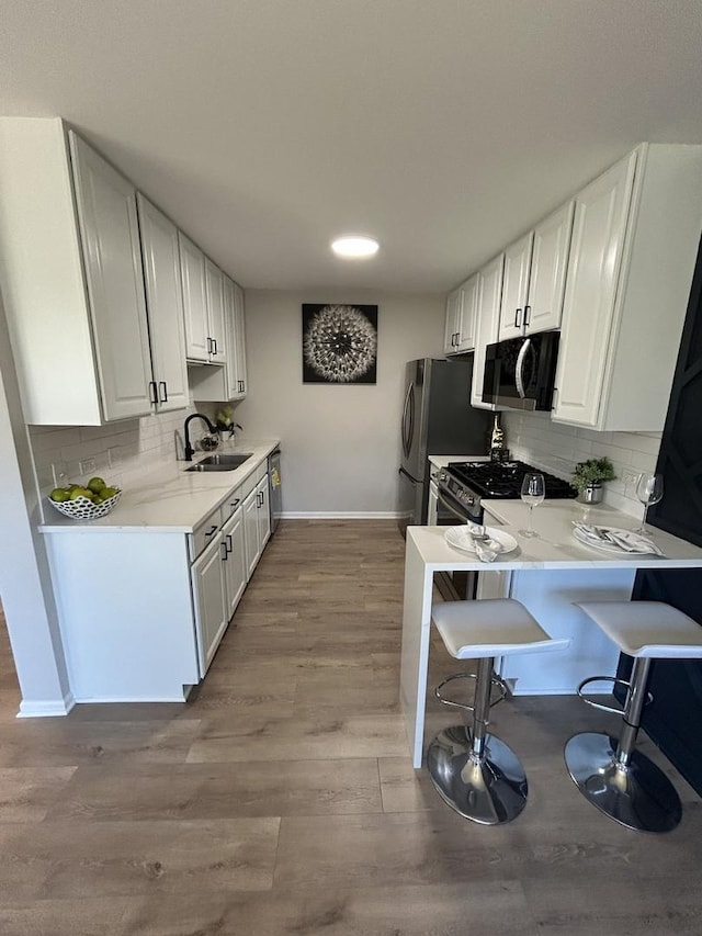 kitchen featuring a sink, a kitchen breakfast bar, stainless steel appliances, white cabinets, and light wood finished floors