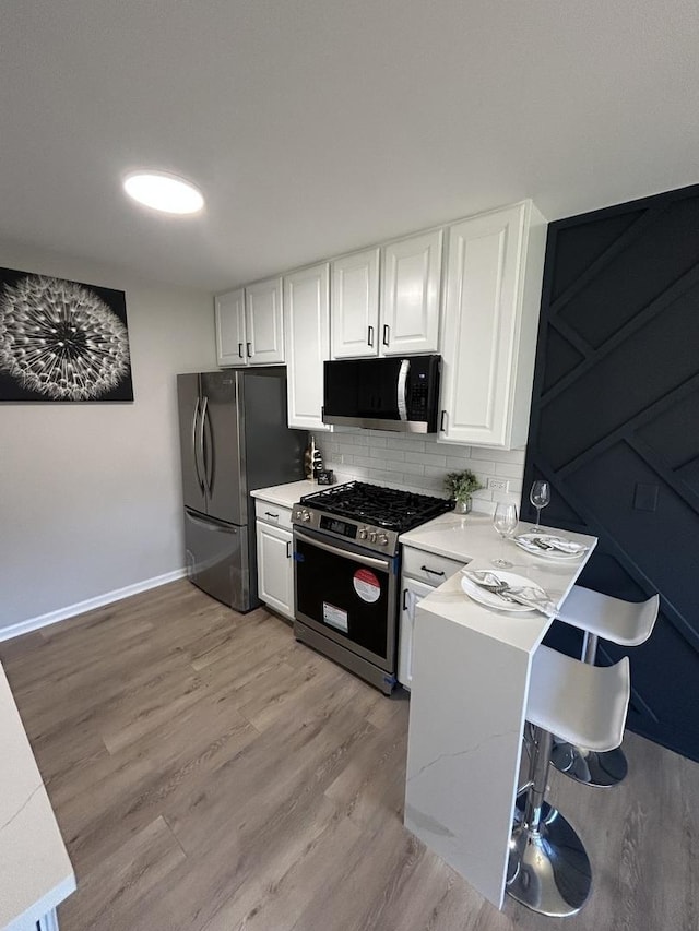 kitchen featuring light wood finished floors, stainless steel appliances, decorative backsplash, light countertops, and white cabinetry