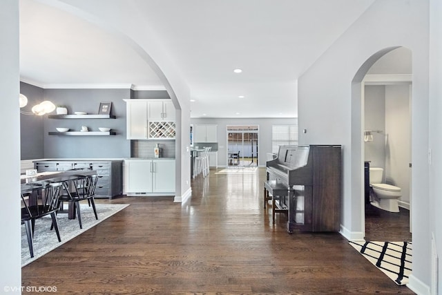 corridor with dark wood-style floors, arched walkways, and baseboards