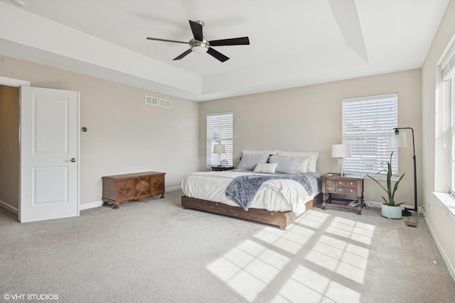 bedroom featuring a tray ceiling, multiple windows, baseboards, and visible vents