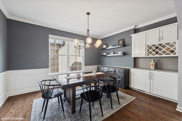 dining room featuring dark wood finished floors, an inviting chandelier, ornamental molding, and wainscoting