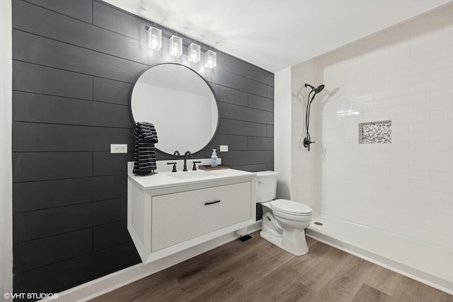 bathroom featuring tiled shower, toilet, wood finished floors, and vanity