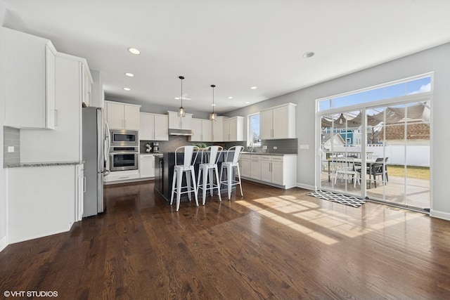 kitchen with under cabinet range hood, backsplash, a center island, stainless steel appliances, and a breakfast bar area