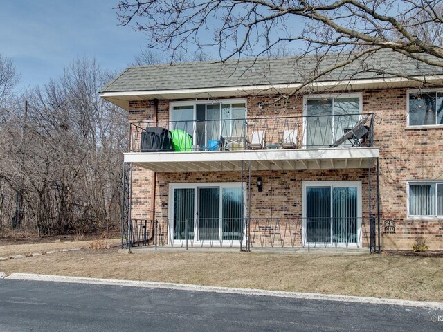 back of house featuring brick siding, a shingled roof, and a balcony