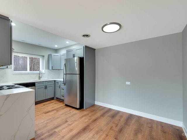 kitchen with gray cabinetry, a sink, freestanding refrigerator, baseboards, and light stone countertops