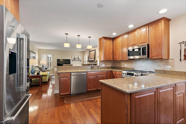 kitchen with dark wood-style floors, a peninsula, a sink, stainless steel appliances, and brown cabinets