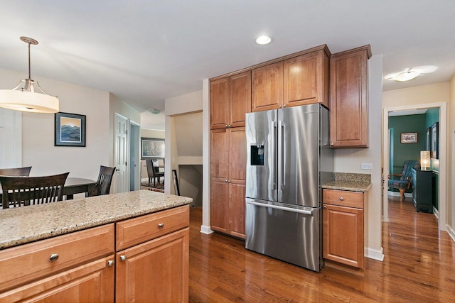 kitchen with brown cabinets, dark wood-type flooring, stainless steel fridge with ice dispenser, and light stone countertops