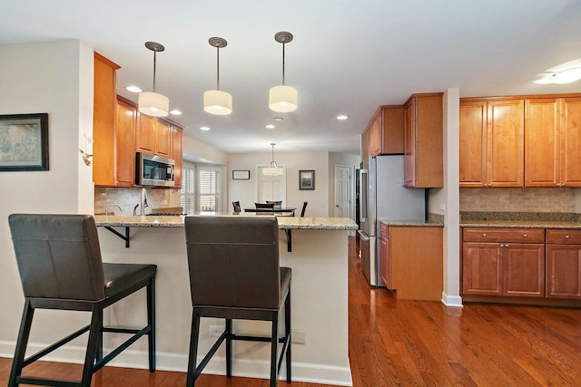 kitchen featuring dark wood-style floors, appliances with stainless steel finishes, a peninsula, and brown cabinetry