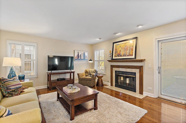 living area featuring a tiled fireplace, baseboards, and wood finished floors