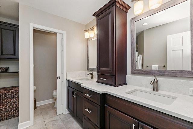 bathroom featuring a sink, baseboards, toilet, and double vanity