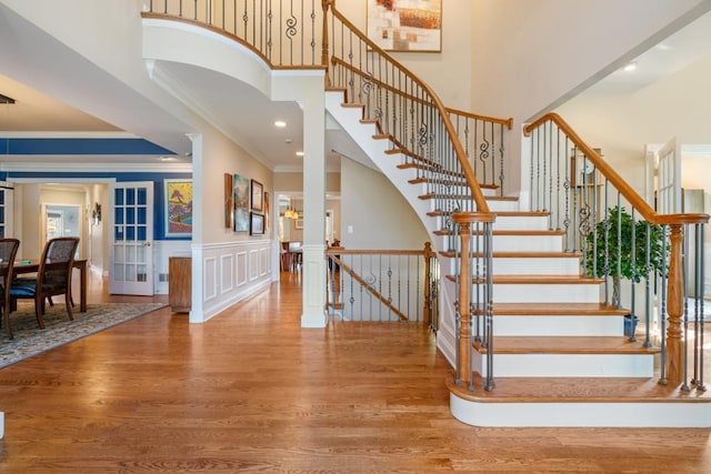 stairs with a decorative wall, wood finished floors, a wainscoted wall, and a towering ceiling