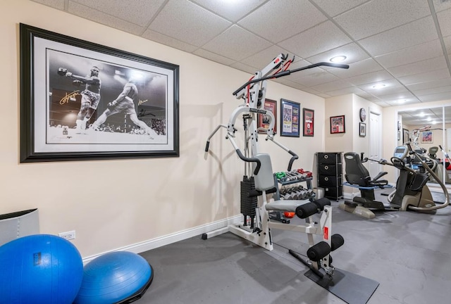 exercise room with baseboards and a drop ceiling